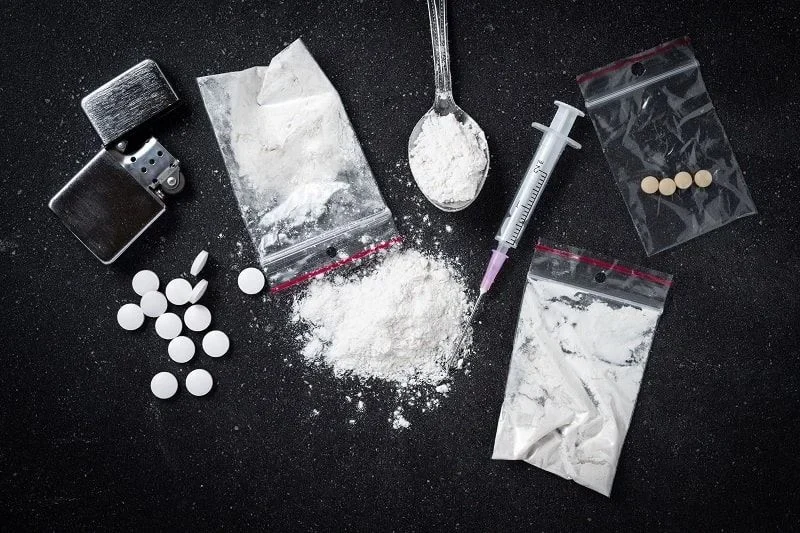 Illegal drugs, pills, powder substances, and a syringe displayed on a table